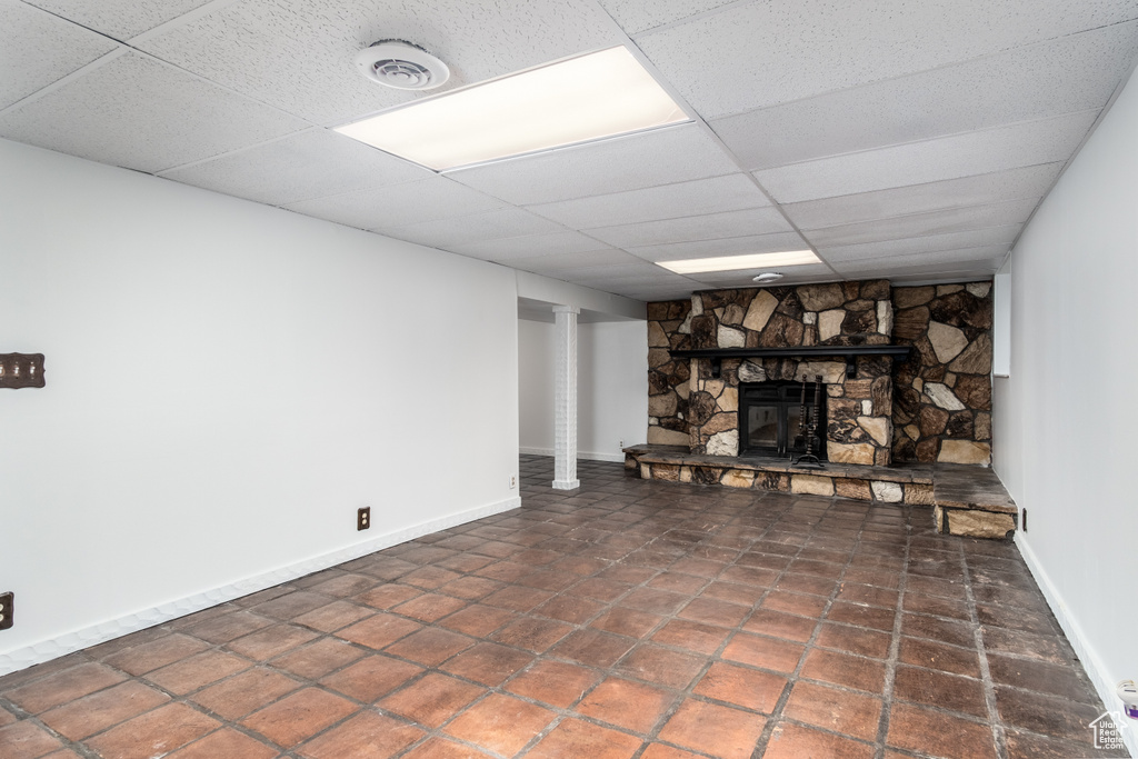Finished basement featuring a stone fireplace, baseboards, and a drop ceiling