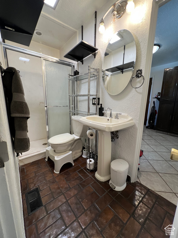 Full bathroom with toilet, a textured wall, a shower stall, and a sink