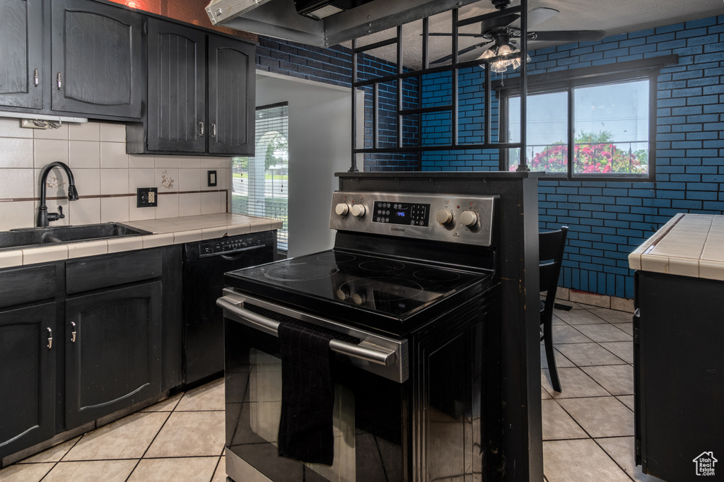 Kitchen featuring stainless steel range with electric cooktop, tile counters, light tile patterned floors, a ceiling fan, and a sink