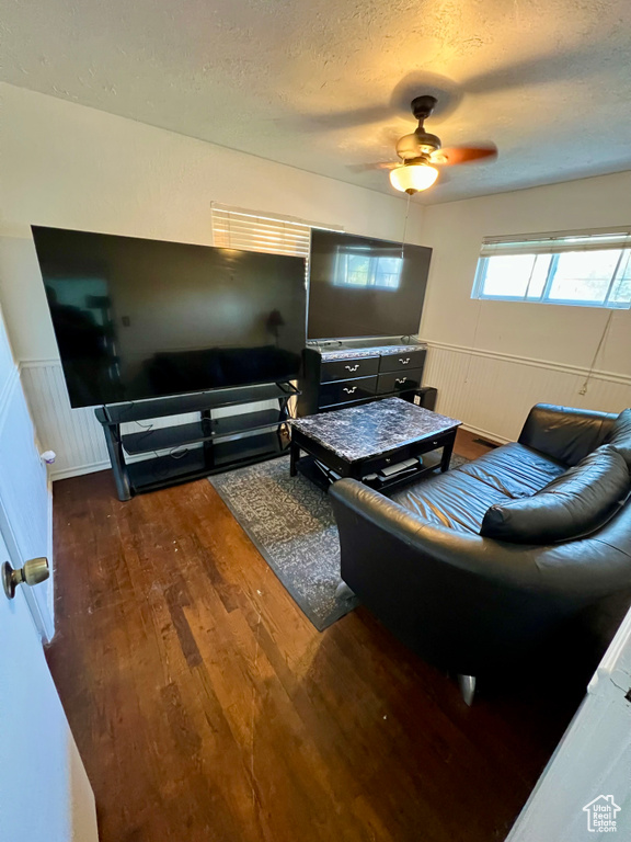 Living room featuring a textured ceiling, wood finished floors, wainscoting, and ceiling fan