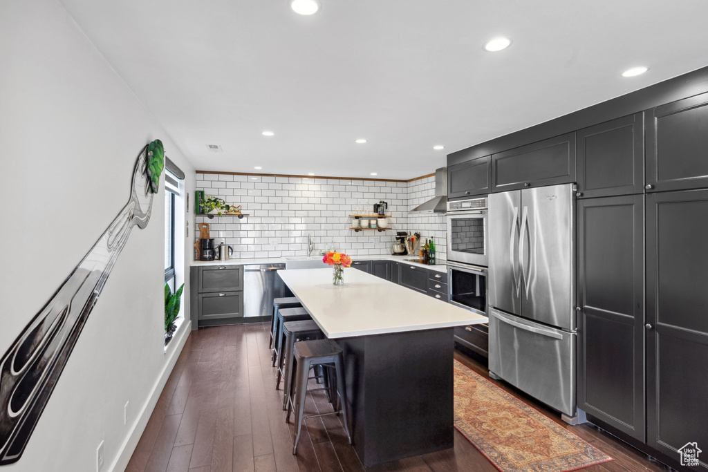 Kitchen with appliances with stainless steel finishes, open shelves, light countertops, a kitchen island, and decorative backsplash