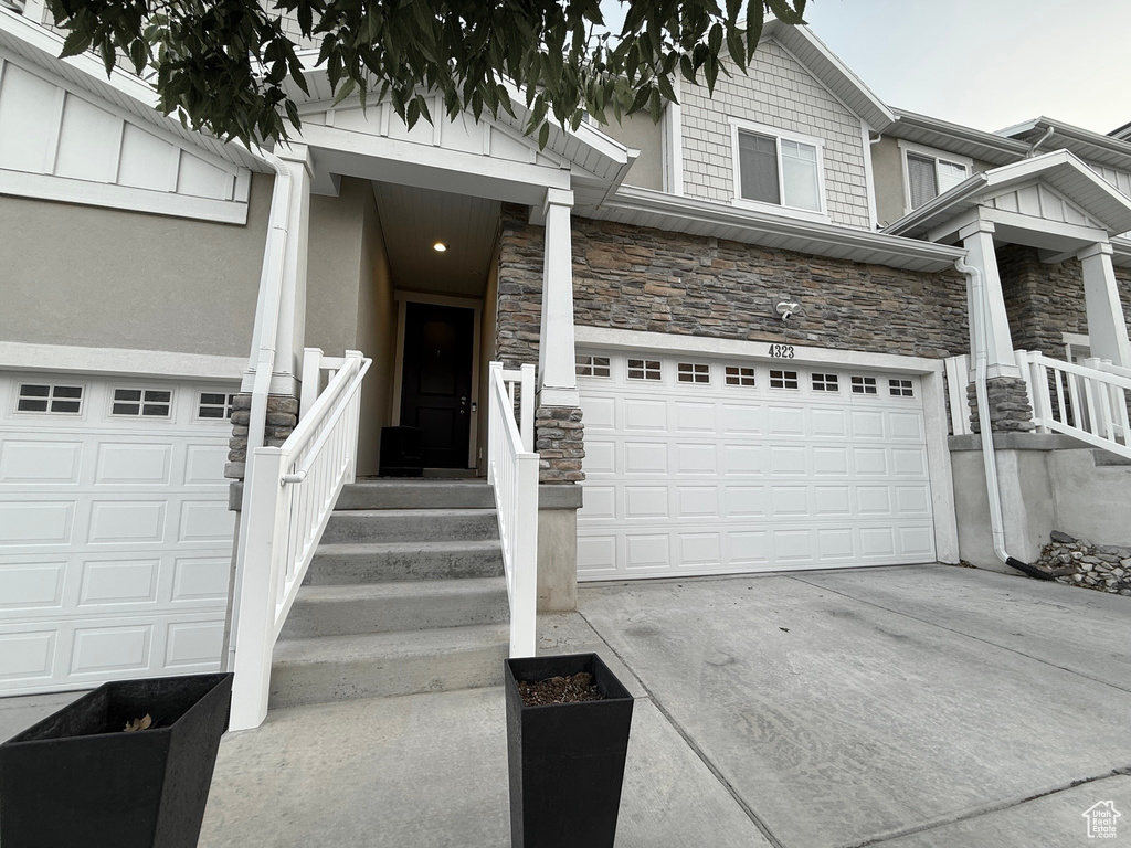 View of front facade with stone siding, an attached garage, driveway, and stucco siding