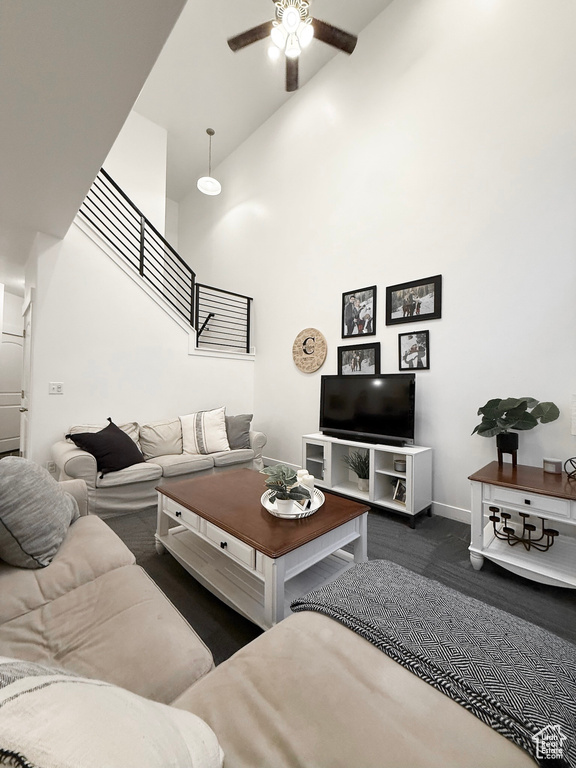 Carpeted living area featuring stairs, ceiling fan, a high ceiling, and baseboards