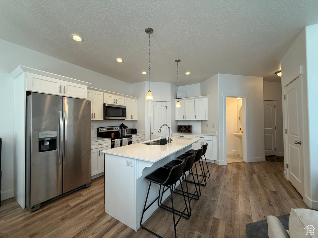 Kitchen with appliances with stainless steel finishes, a sink, dark wood-style flooring, a kitchen bar, and white cabinetry
