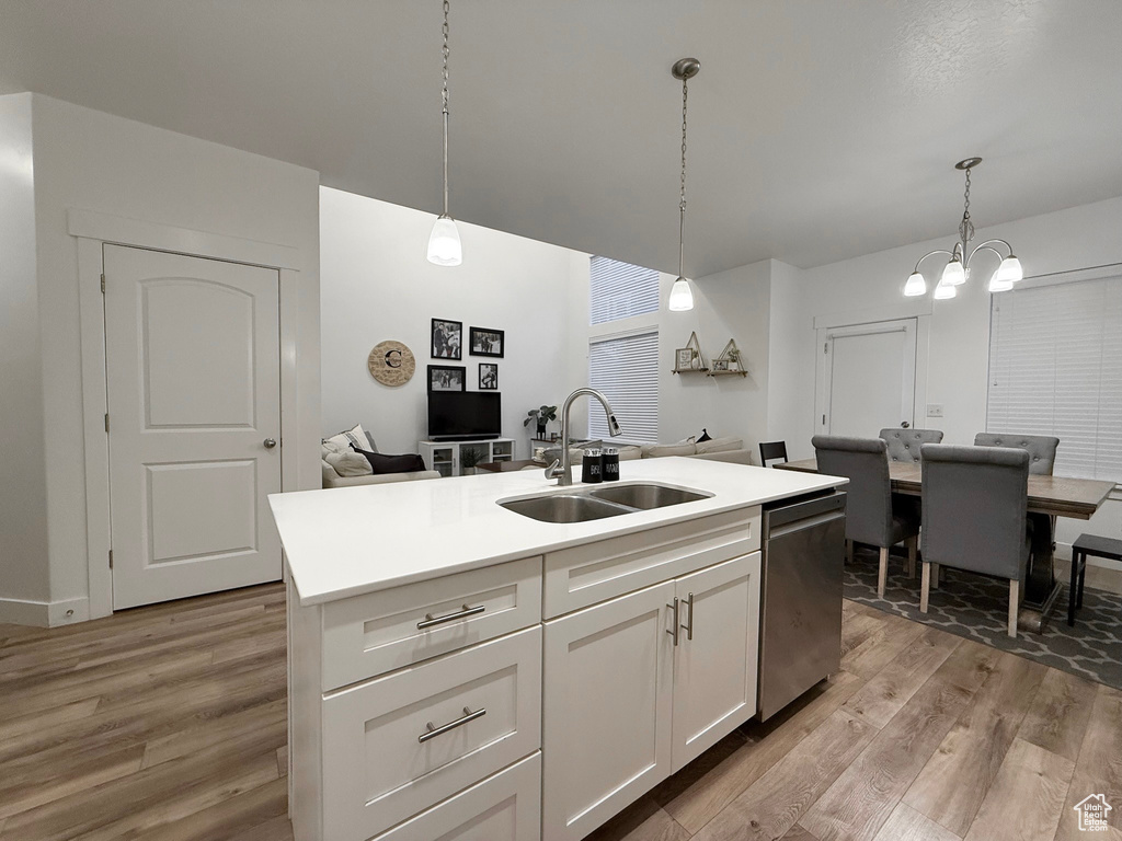 Kitchen with a sink, stainless steel dishwasher, light wood-style floors, white cabinetry, and decorative light fixtures