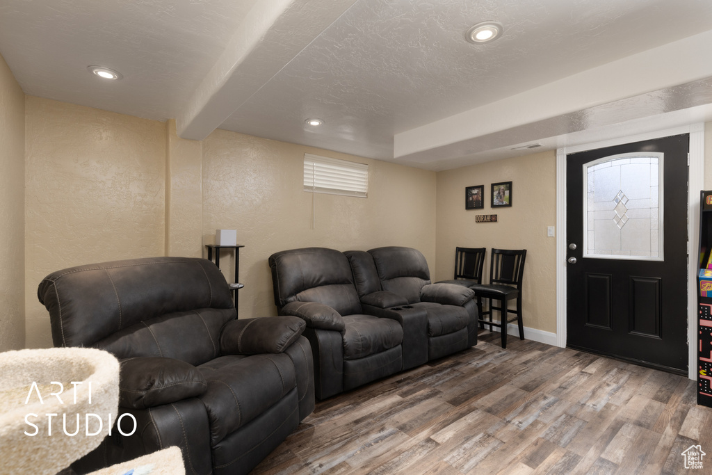 Living room with wood finished floors, a textured wall, recessed lighting, baseboards, and beamed ceiling