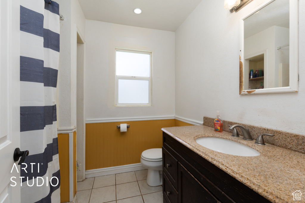 Full bath with vanity, toilet, wainscoting, tile patterned floors, and baseboards