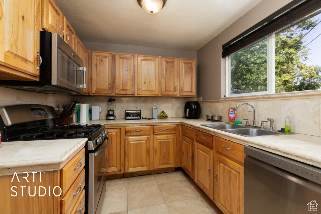 Kitchen with appliances with stainless steel finishes, a sink, light countertops, tasteful backsplash, and light tile patterned flooring