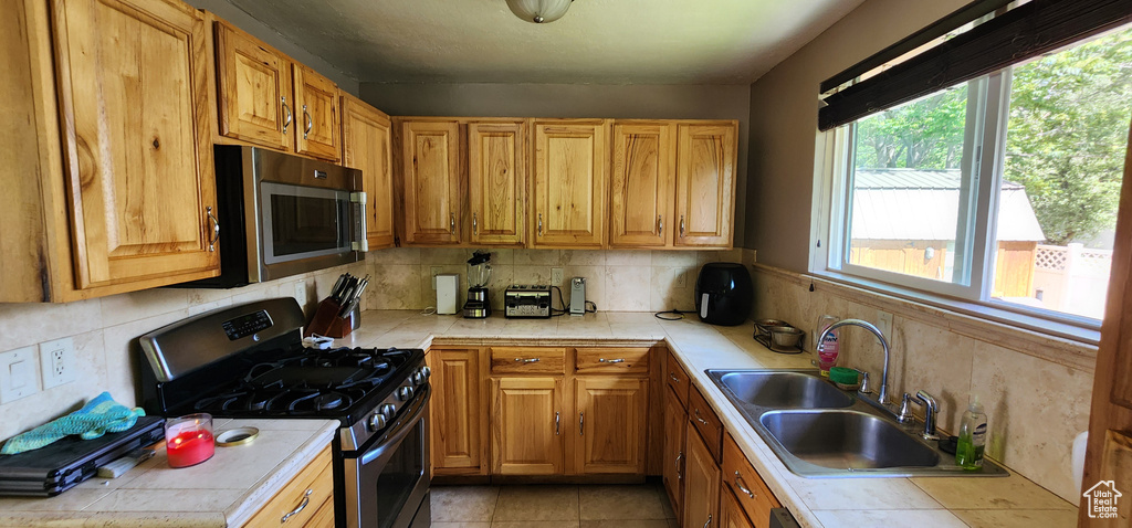 Kitchen with stainless steel appliances, tile counters, a sink, and decorative backsplash
