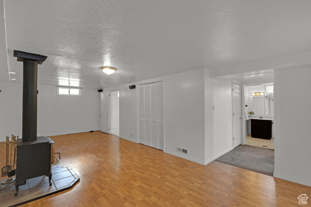 Unfurnished living room with wood finished floors, a wood stove, a textured ceiling, and baseboards