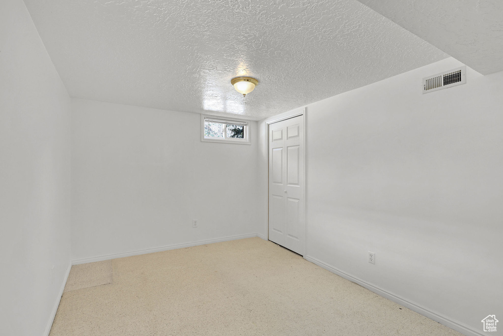 Below grade area with a textured ceiling, baseboards, and light colored carpet