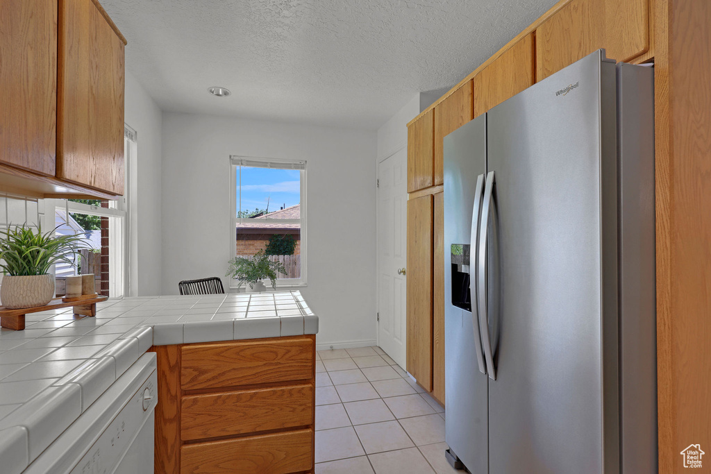 Kitchen featuring stainless steel fridge with ice dispenser, white dishwasher, tile countertops, a textured ceiling, and light tile patterned flooring
