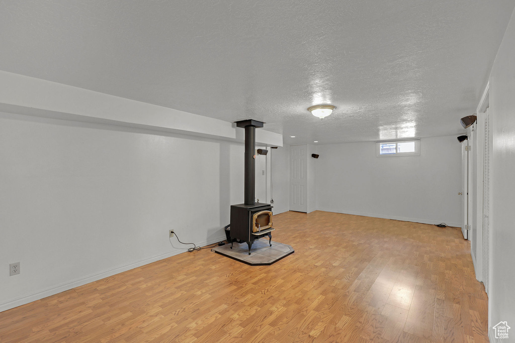 Below grade area with light wood-style floors, a wood stove, a textured ceiling, and baseboards