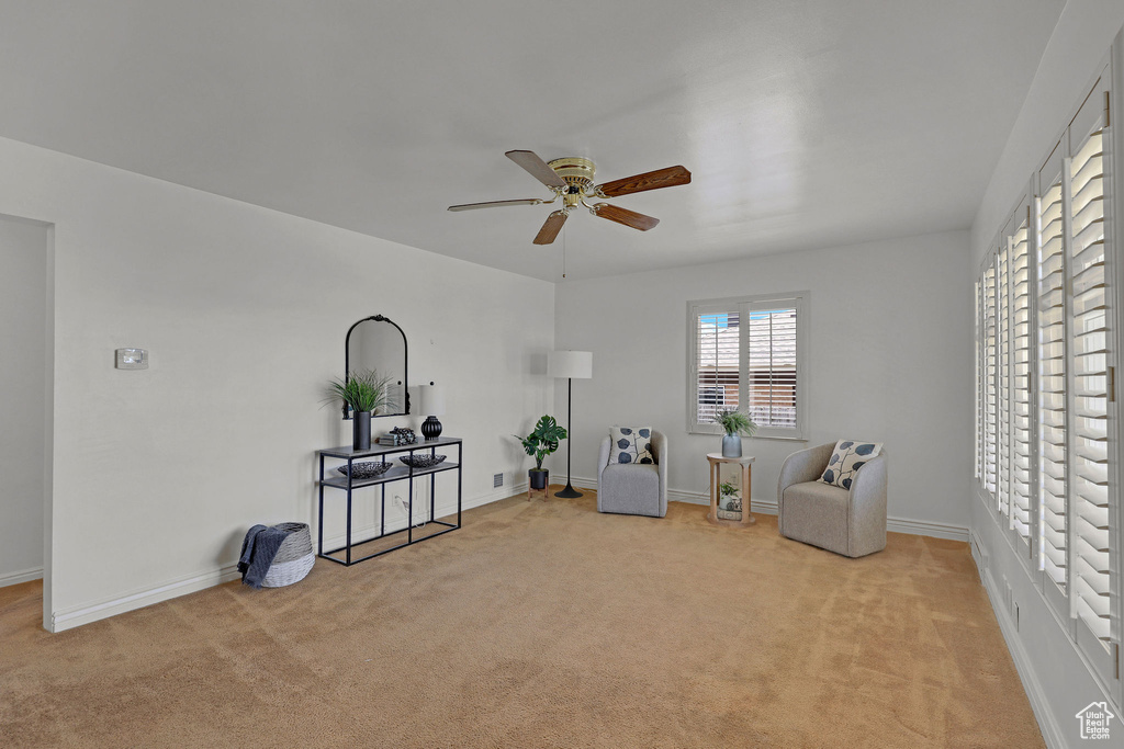 Living area with a ceiling fan, light colored carpet, and baseboards