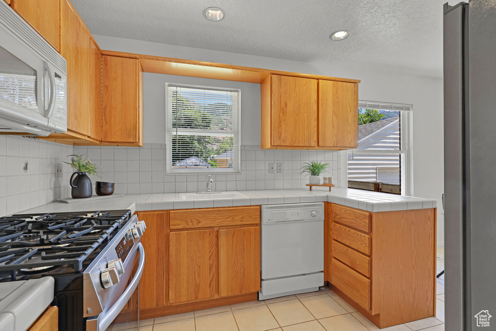 Kitchen with white appliances, a sink, healthy amount of natural light, tasteful backsplash, and a textured ceiling
