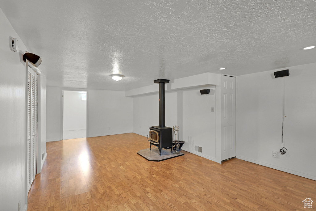 Below grade area with a textured ceiling, light wood finished floors, a wood stove, and baseboards