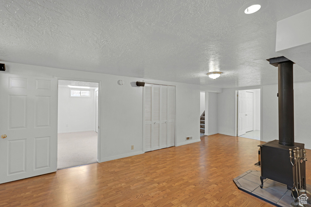 Unfurnished living room featuring a textured ceiling, wood finished floors, stairway, a wood stove, and baseboards