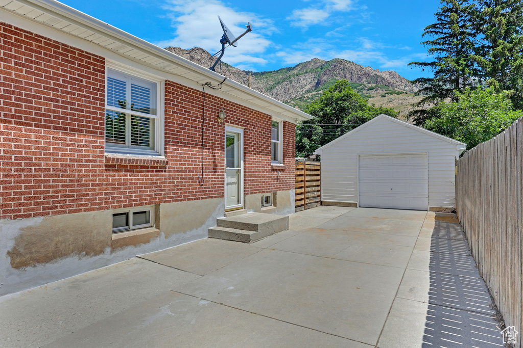 View of property exterior with a mountain view, concrete driveway, a garage, an outdoor structure, and brick siding