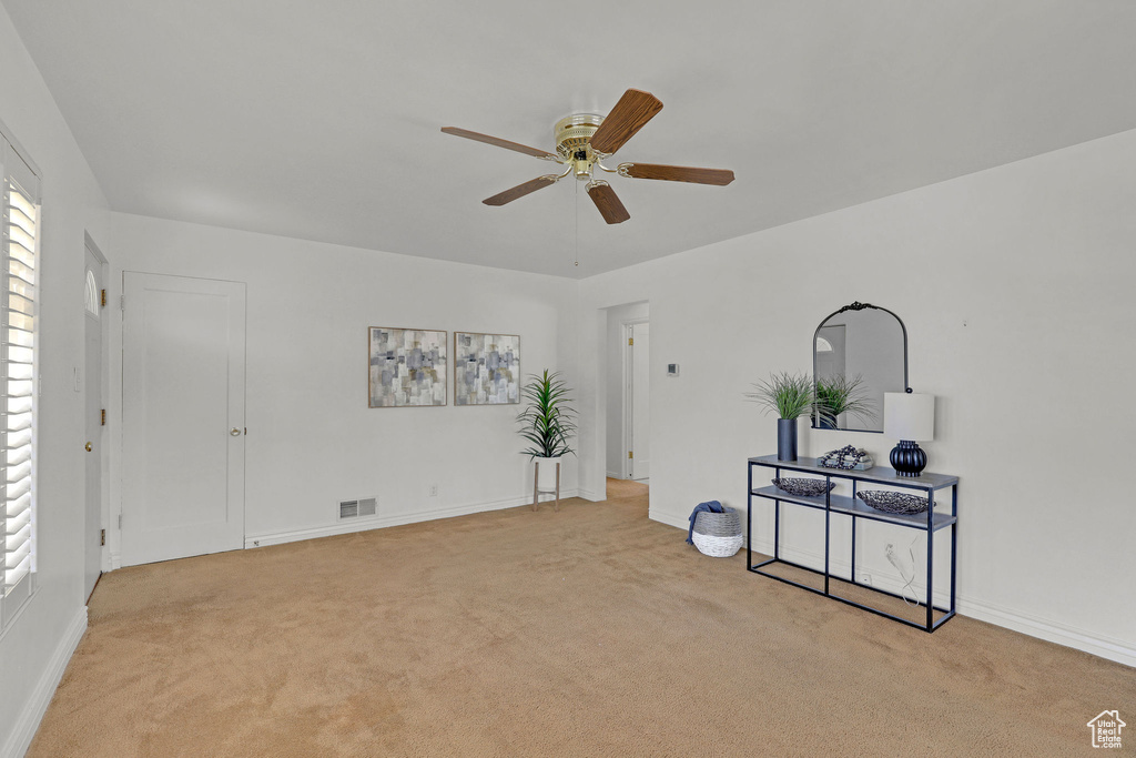 Unfurnished living room featuring light colored carpet, ceiling fan, and baseboards