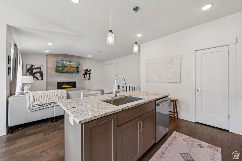 Kitchen featuring a sink, dishwasher, dark wood-style floors, a fireplace, and hanging light fixtures