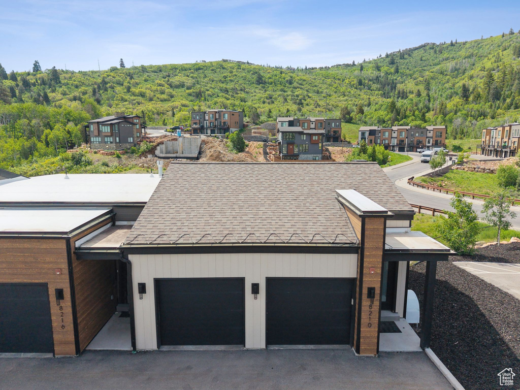 View of front facade with a wooded view, an attached garage, driveway, and roof with shingles