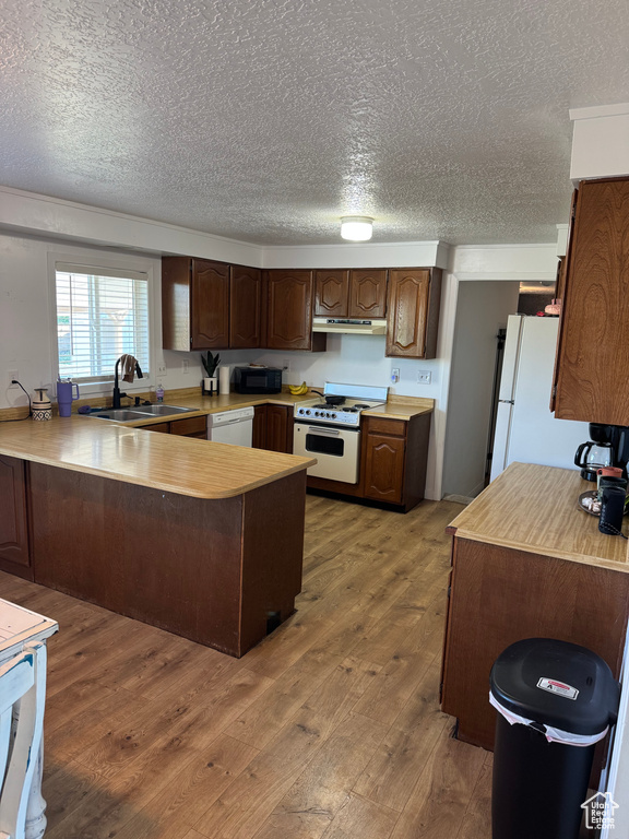 Kitchen featuring white appliances, a peninsula, hardwood / wood-style flooring, a textured ceiling, and light countertops