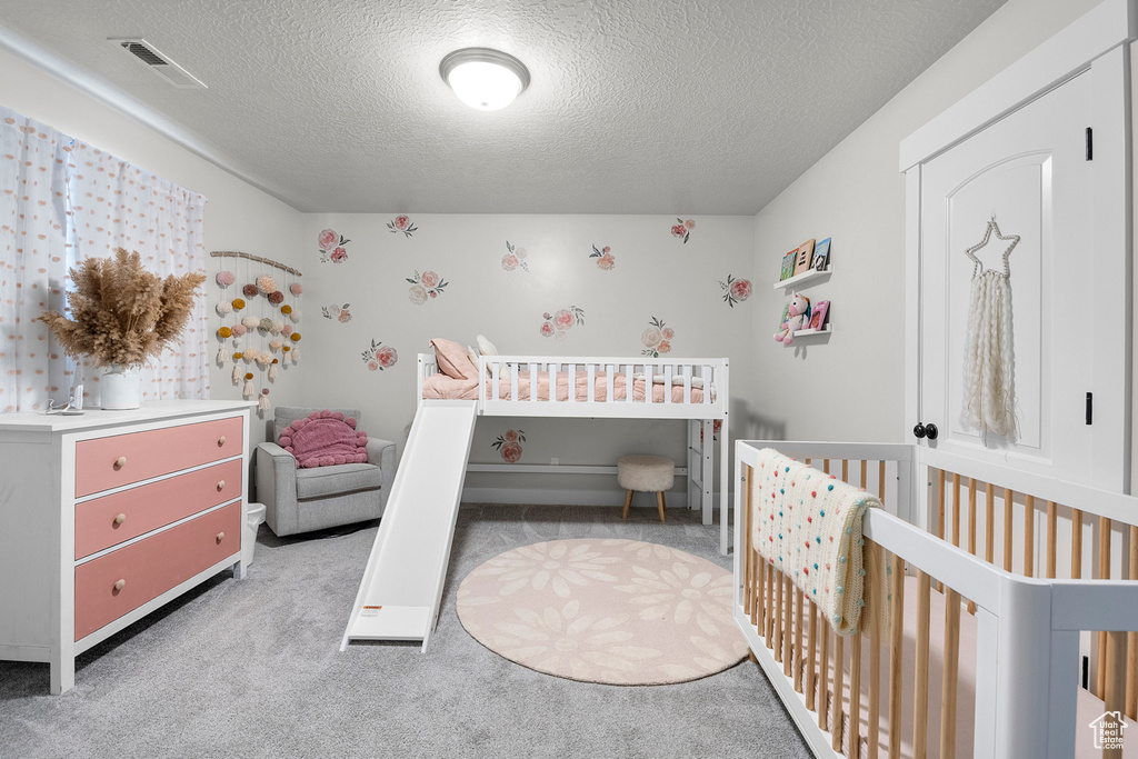 Carpeted bedroom featuring a crib and a textured ceiling