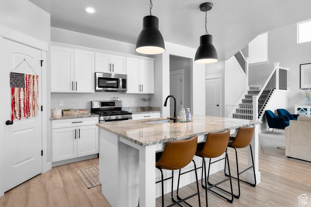 Kitchen with appliances with stainless steel finishes, light stone countertops, light wood-type flooring, a sink, and a kitchen bar
