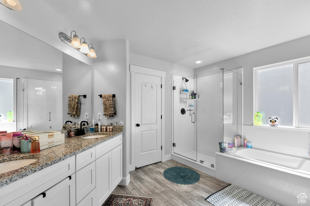 Bathroom featuring a stall shower, wood finished floors, a garden tub, double vanity, and plenty of natural light