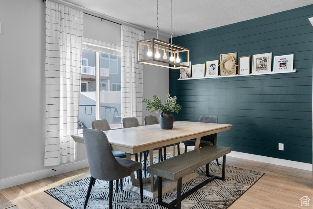 Dining area with baseboards, a chandelier, wood finished floors, and wooden walls