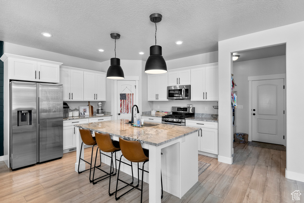 Kitchen featuring appliances with stainless steel finishes, a sink, light wood-type flooring, white cabinets, and light stone counters