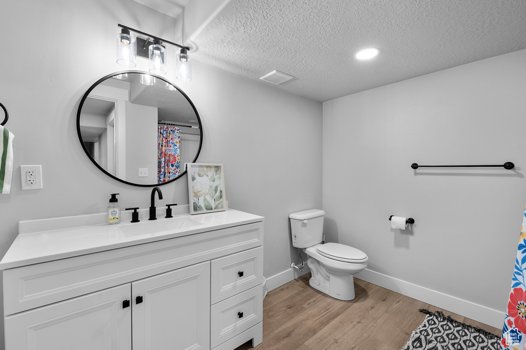Full bathroom featuring vanity, toilet, wood finished floors, a textured ceiling, and baseboards