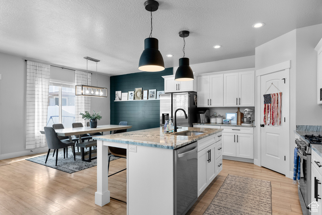 Kitchen with stainless steel appliances, a sink, light wood-style floors, white cabinets, and a kitchen island with sink