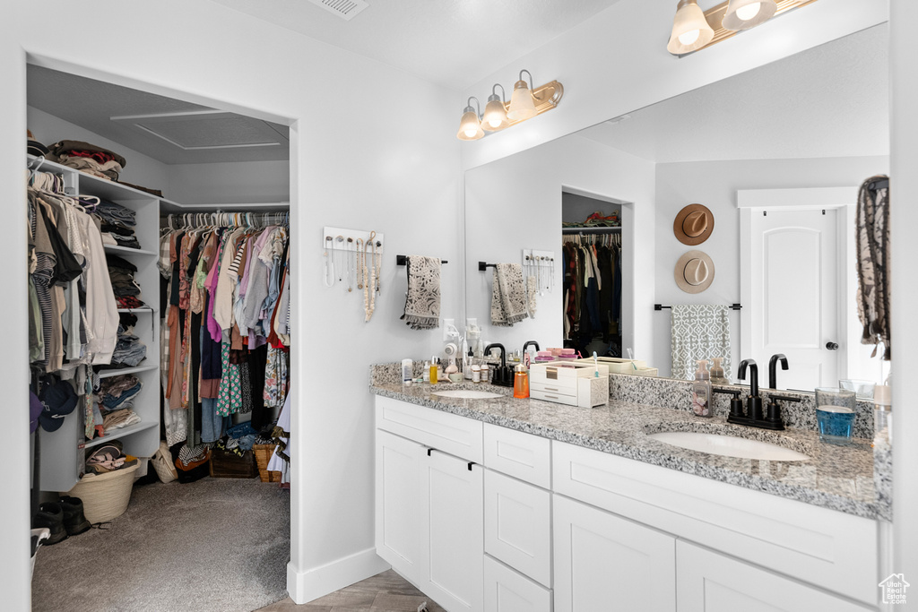 Full bathroom with double vanity, a walk in closet, and baseboards