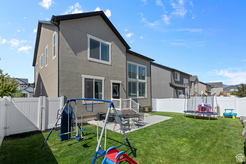 Rear view of house featuring a gate, stucco siding, a residential view, a patio, and a trampoline