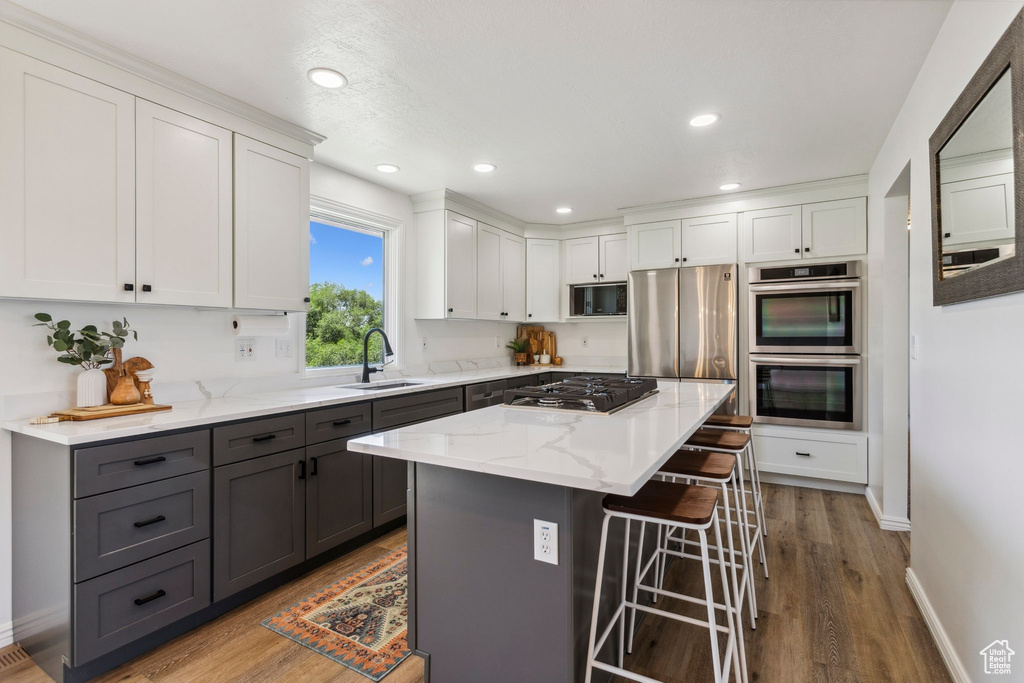 Kitchen with gray cabinets, appliances with stainless steel finishes, a breakfast bar area, white cabinets, and a sink