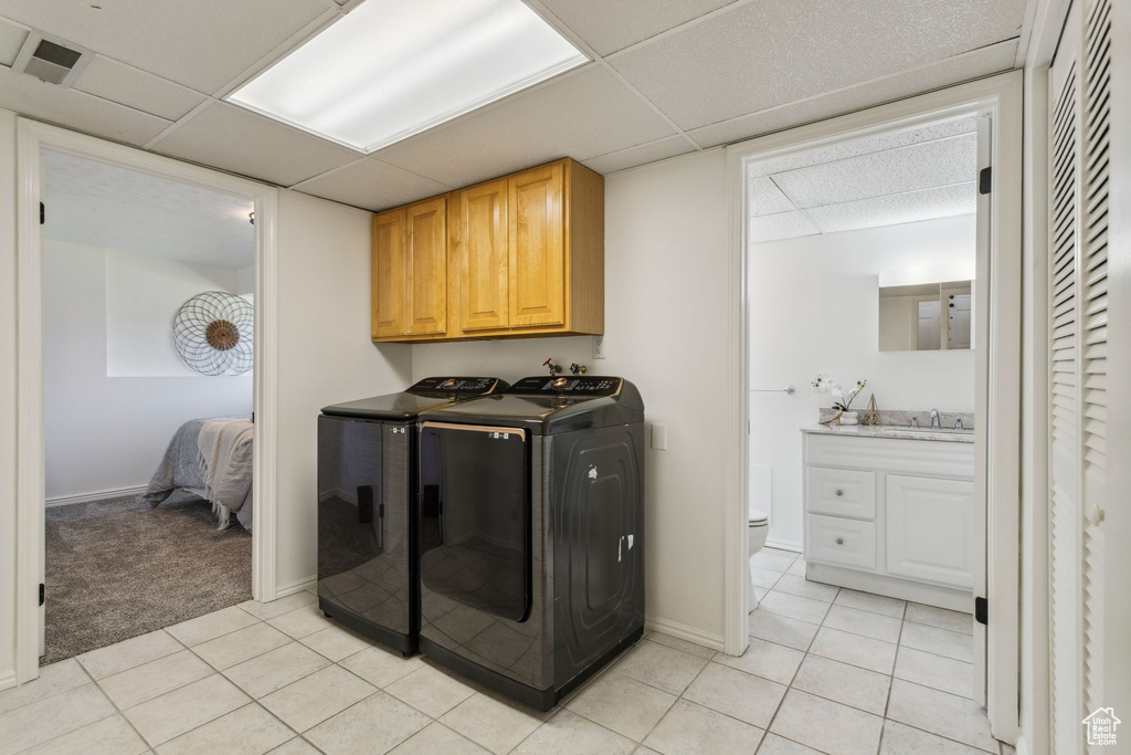 Laundry room featuring washer and dryer, light tile patterned flooring, cabinet space, and baseboards
