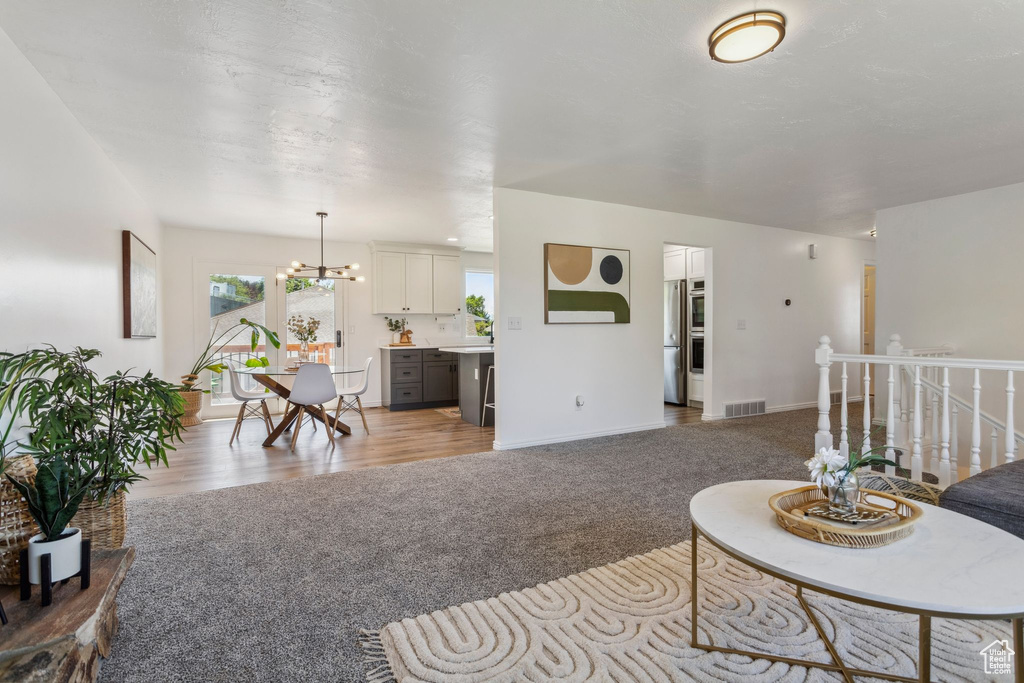 Carpeted living room with a chandelier, wood finished floors, and baseboards