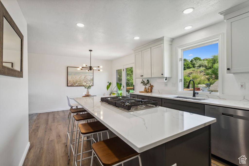 Kitchen with stainless steel appliances, a sink, a center island, light stone countertops, and wood finished floors