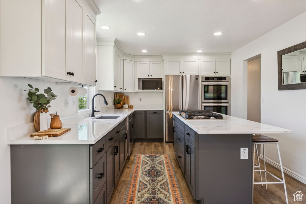 Kitchen with a sink, stainless steel appliances, gray cabinets, wood finished floors, and a kitchen island