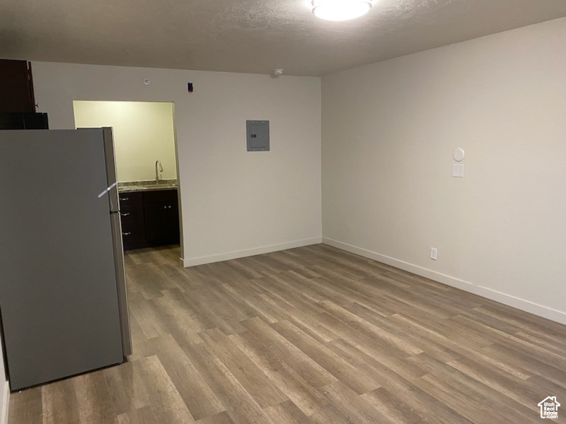 Empty room with a sink, light wood finished floors, electric panel, and baseboards