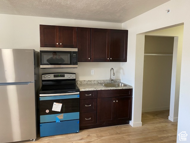 Kitchen featuring appliances with stainless steel finishes, a sink, light wood-style flooring, dark brown cabinetry, and a textured ceiling