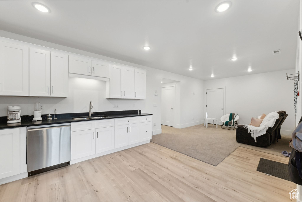 Kitchen featuring stainless steel dishwasher, a sink, dark countertops, light wood-style flooring, and recessed lighting