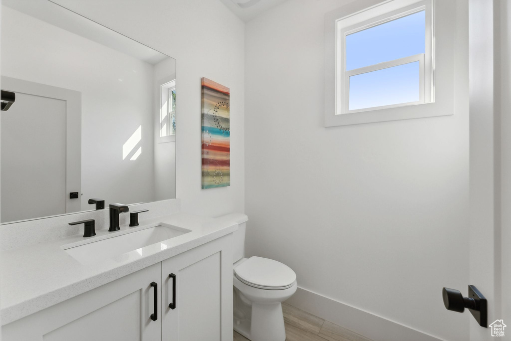 Half bathroom featuring healthy amount of natural light, vanity, toilet, and baseboards
