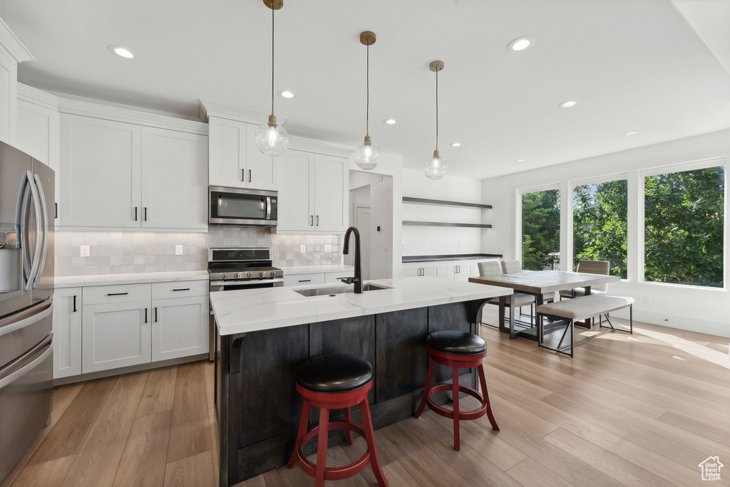 Kitchen with stainless steel appliances, a sink, decorative backsplash, white cabinetry, and recessed lighting