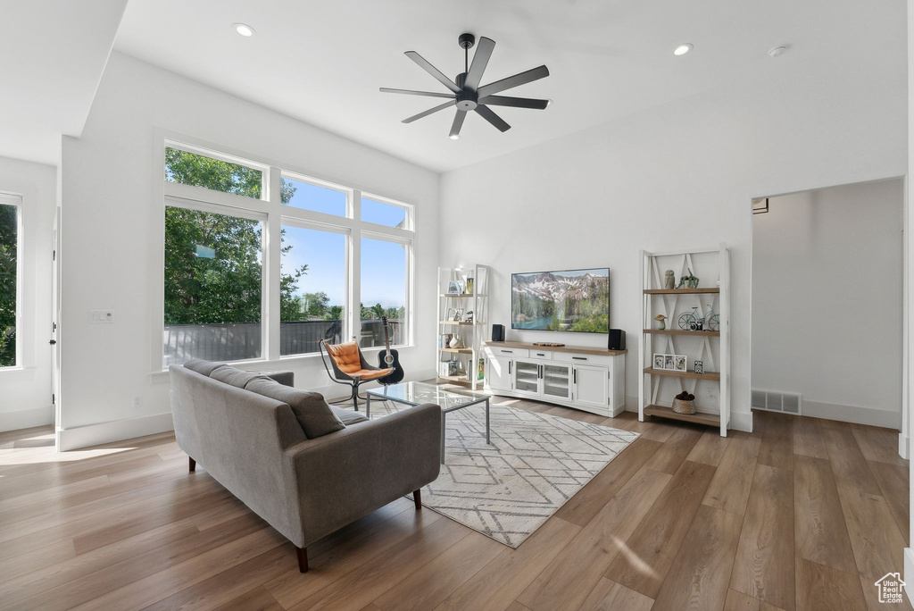 Living area featuring ceiling fan, wood finished floors, recessed lighting, baseboards, and a high ceiling