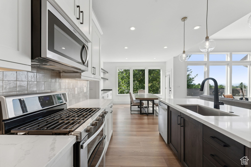 Kitchen with appliances with stainless steel finishes, a sink, recessed lighting, light wood-type flooring, and white cabinetry