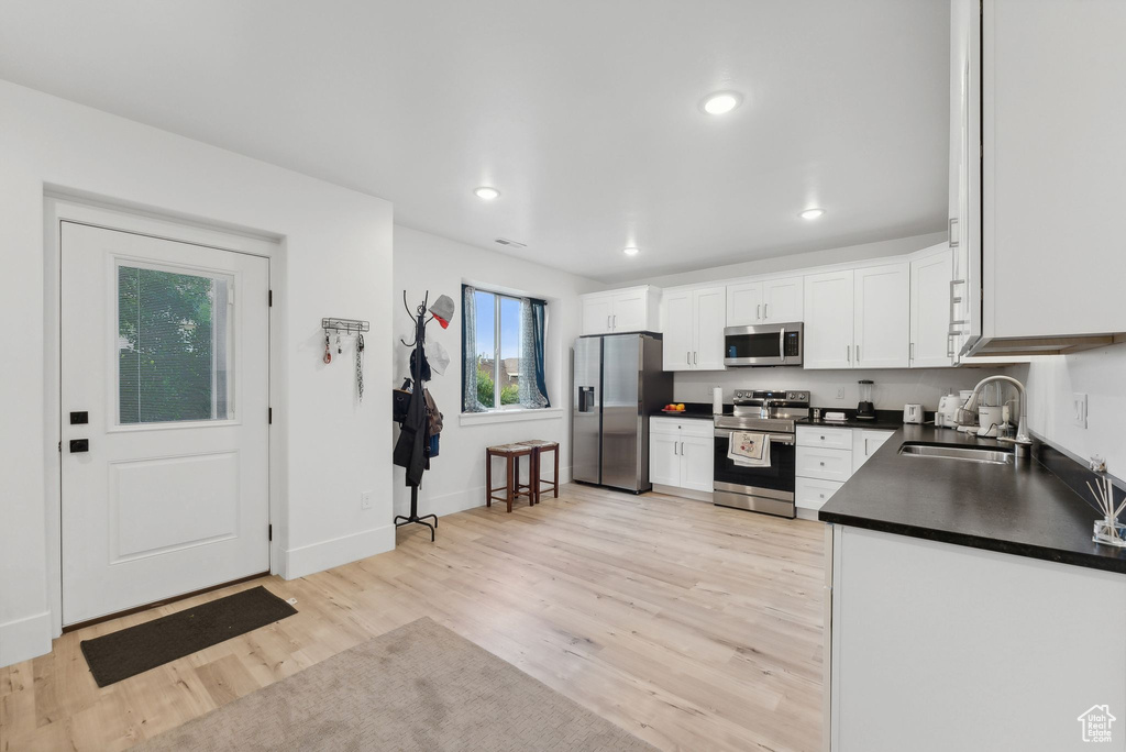Kitchen with stainless steel appliances, a sink, dark countertops, white cabinetry, and light wood-type flooring