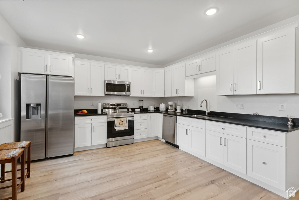 Kitchen with stainless steel appliances, a sink, white cabinets, dark countertops, and recessed lighting