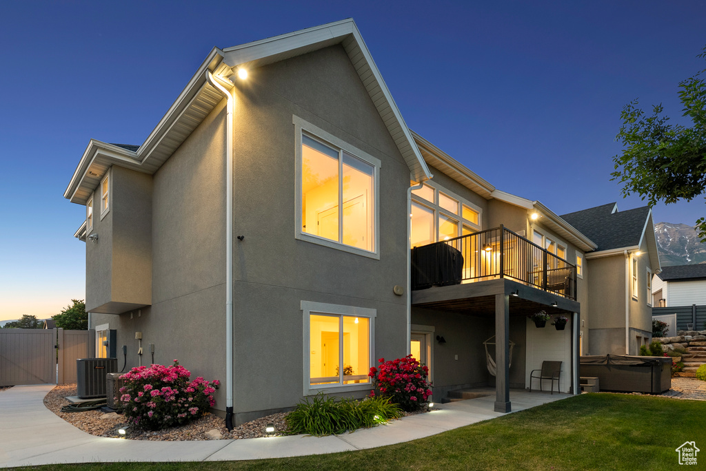 Rear view of house with a hot tub, stucco siding, a balcony, a gate, and a patio area